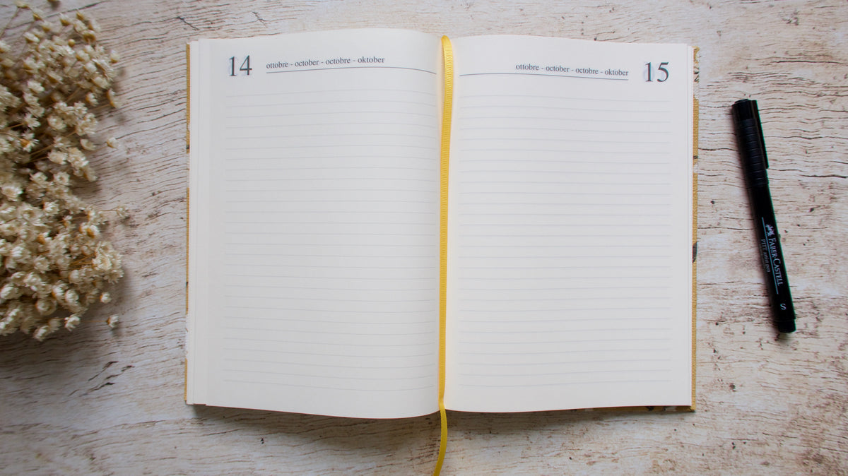 Agenda perpétuel ouvert à plat sur un bureau, une page par jour, avec marque page